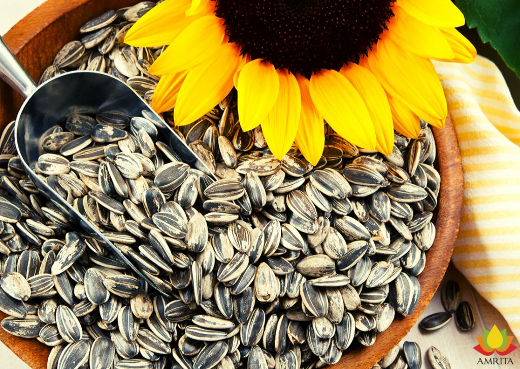 A wooden bowl filled with sunflower seeds on a table next to a sunflower with a yellow and white striped napkin